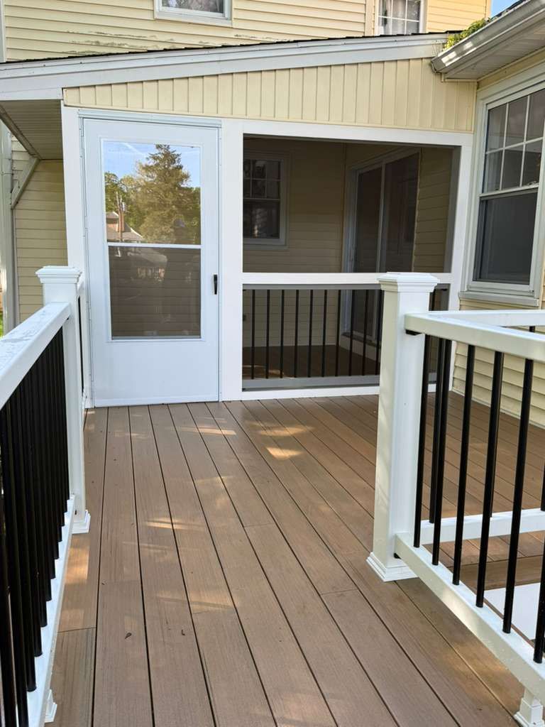 Wooden porch deck with white railing and screened door beside a beige house