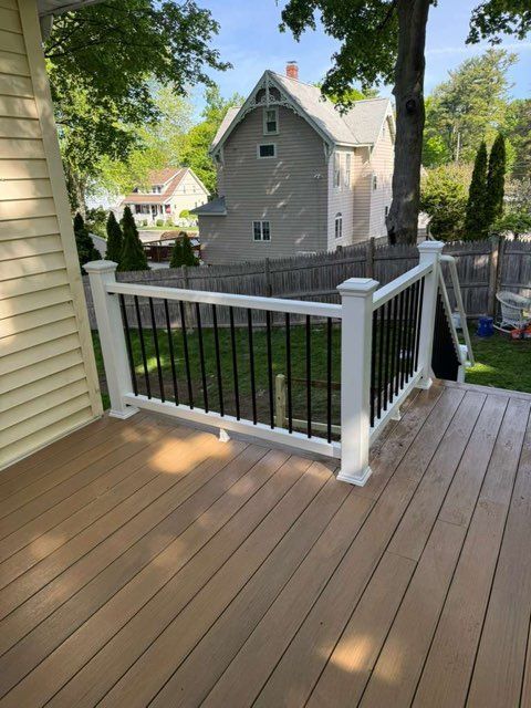 Wood deck with white railing overlooking a fenced backyard and gray house