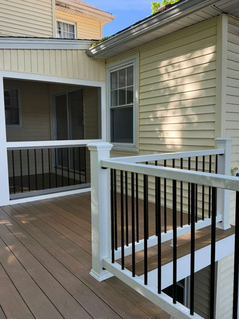 Wooden deck walkway beside a house with white railings and black balusters in sunlight