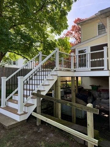 White-railed outdoor staircase to a raised deck beside a beige house with trees and support beams below