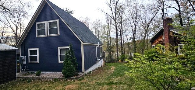 Blue house with a steep roof in a wooded yard, with a smaller cabin and chimney in the background