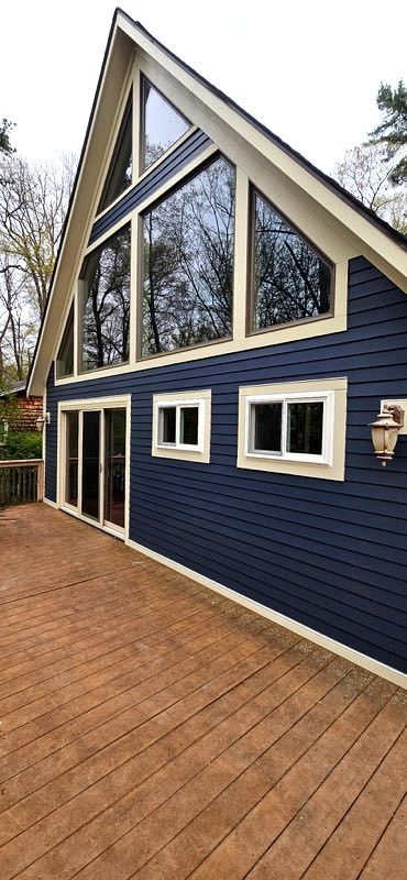 Blue house with steep gabled roof, large triangular windows, and a brick patio in front