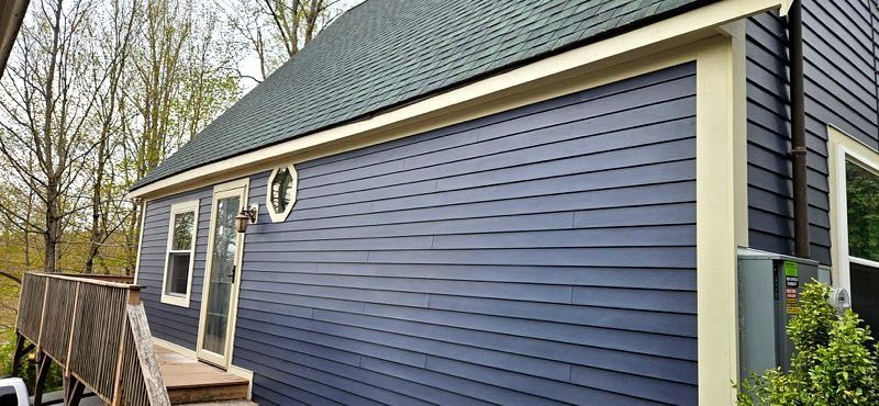 Blue-sided house exterior with a small porch and wooded yard around it