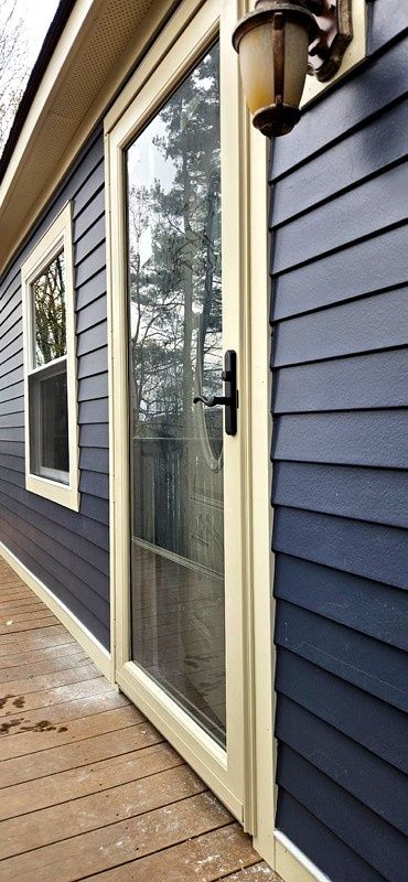 Wooden deck beside a blue house with a glass sliding door and wall lantern