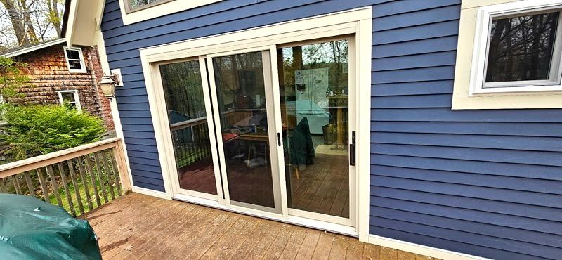 Blue house exterior with white sliding glass doors opening onto a wooden deck