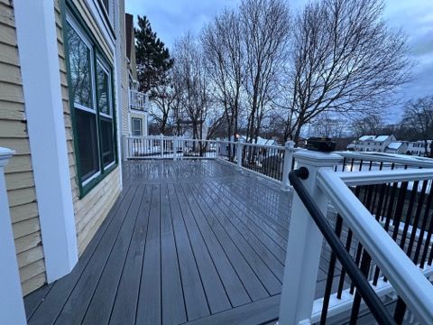 A grey wooden deck with white railings overlooks a wintry, tree-filled landscape under a cloudy sky.