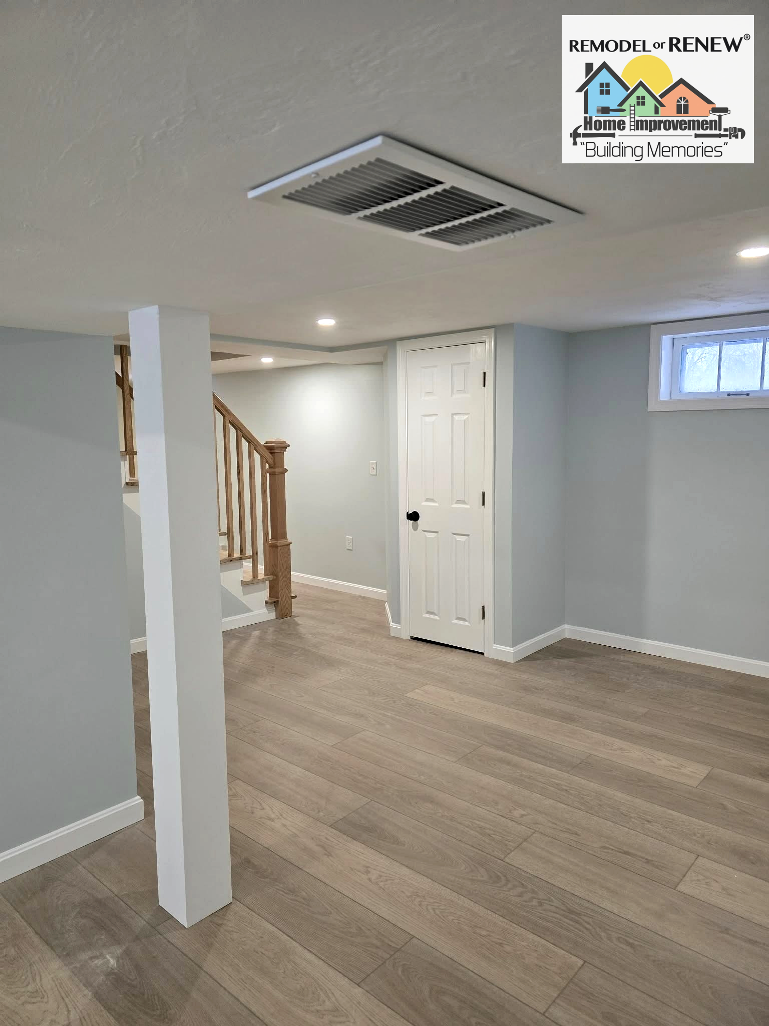 A renovated basement featuring light gray walls, wood-look flooring, a white pillar, a white closet door, and a staircase.