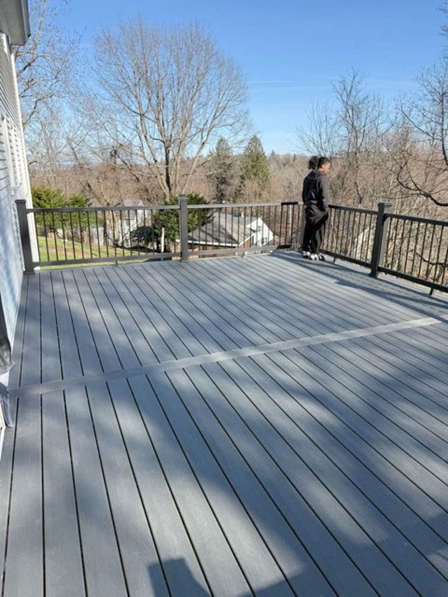 A gray wooden deck overlooking a wooded landscape under a clear blue sky
