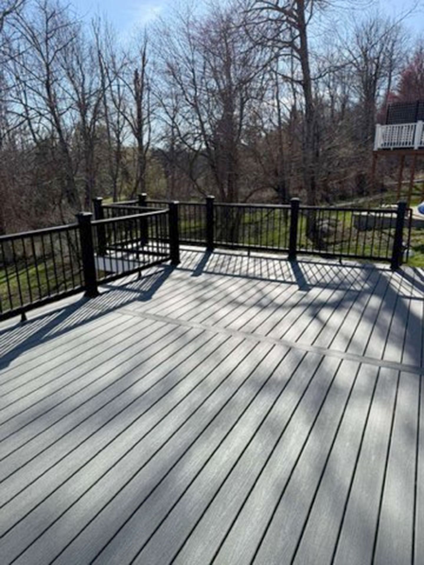 A gray composite deck with black metal railing overlooking a wooded backyard