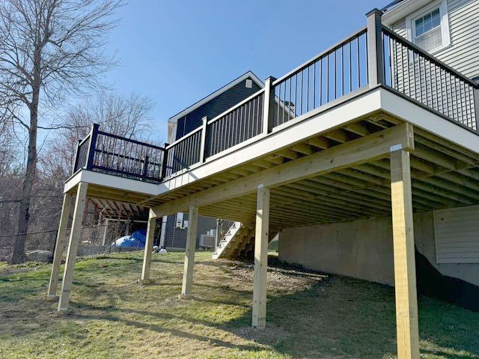 A wooden deck attached to a house with black railings, supported by wooden posts