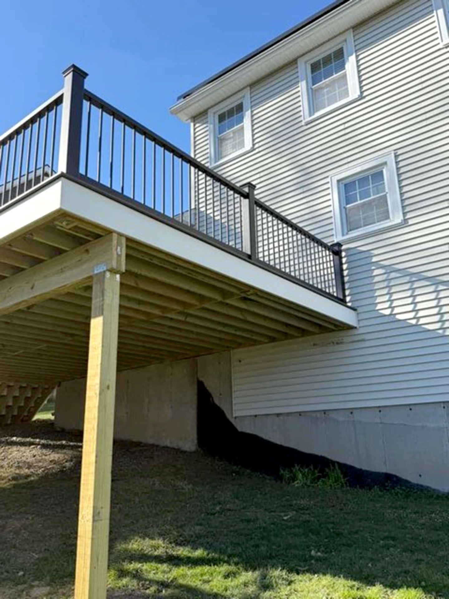 A raised wooden deck with black railings attached to the side of a light-colored, vinyl-sided house
