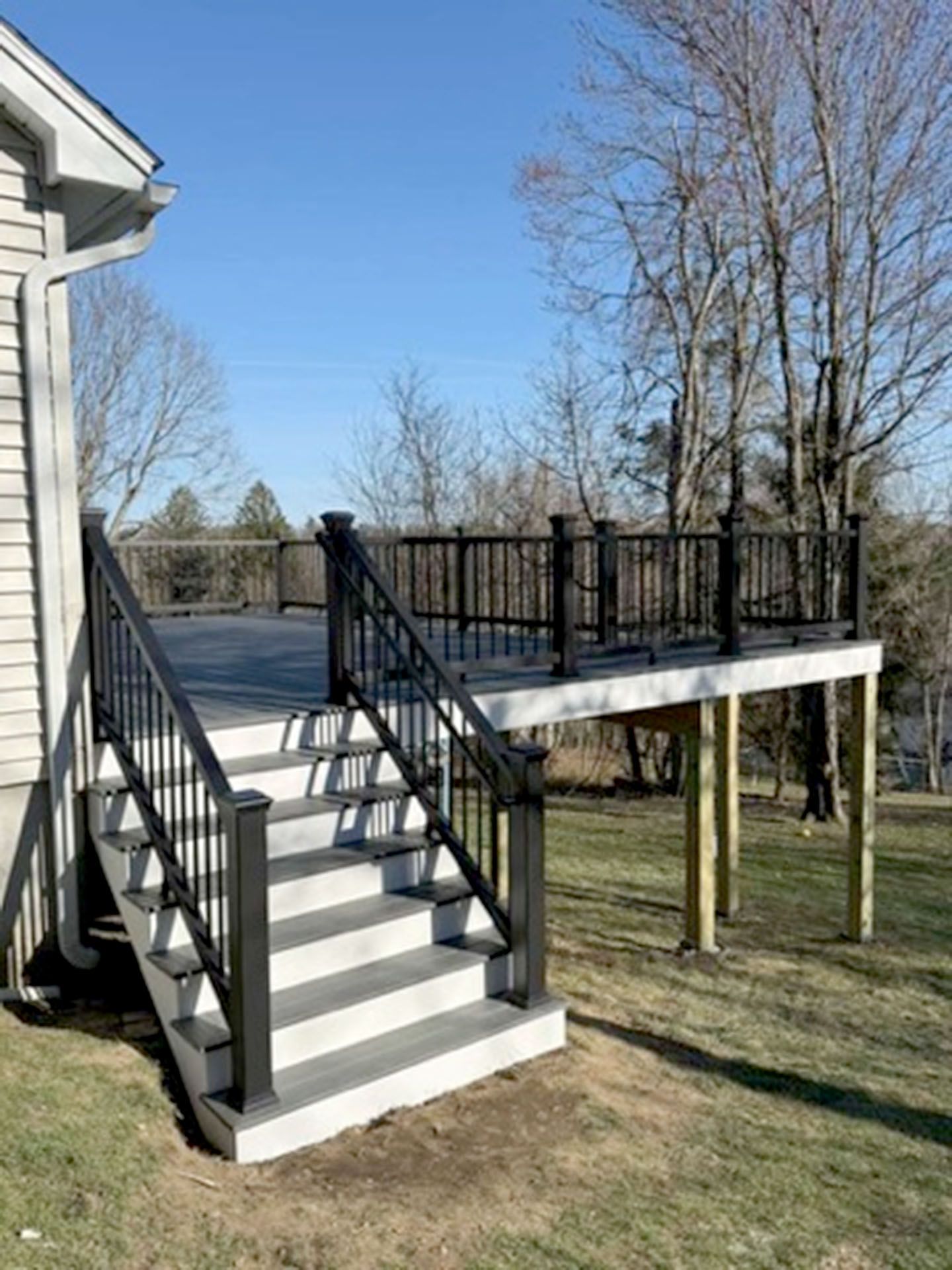 A raised deck with gray composite decking, black railings, and a set of matching stairs 