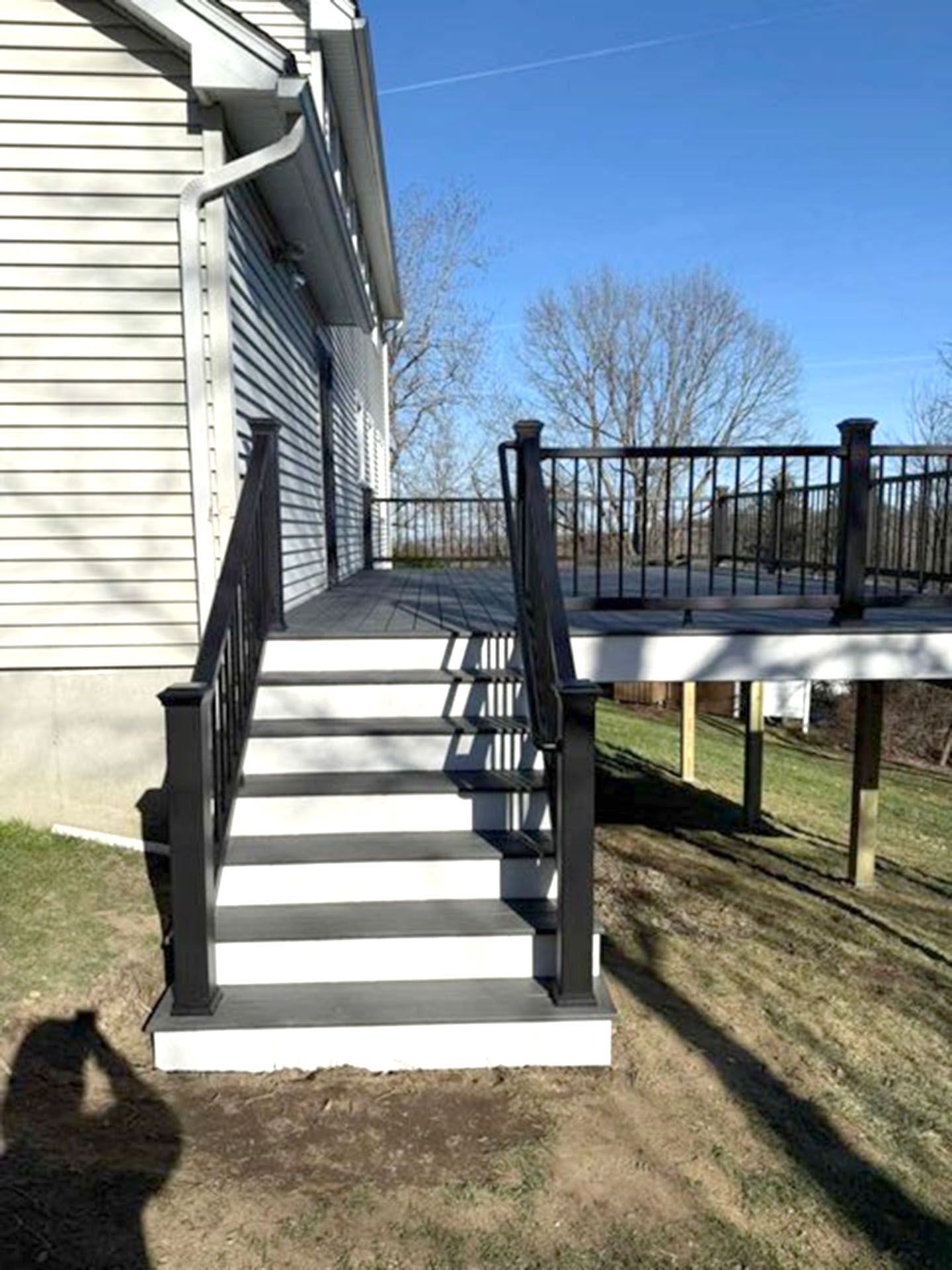 A set of stairs with white risers and gray treads leading up to a deck with black railings