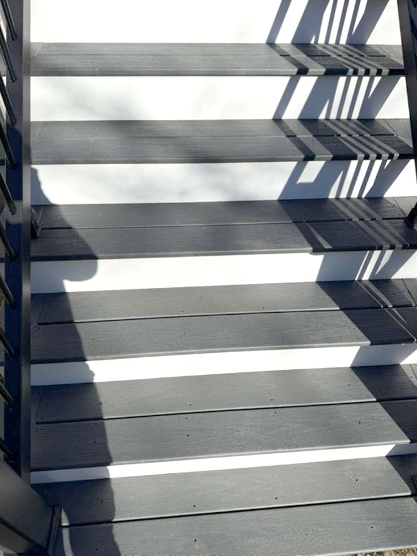 A stairs with dark gray composite treads, white risers, and black railings