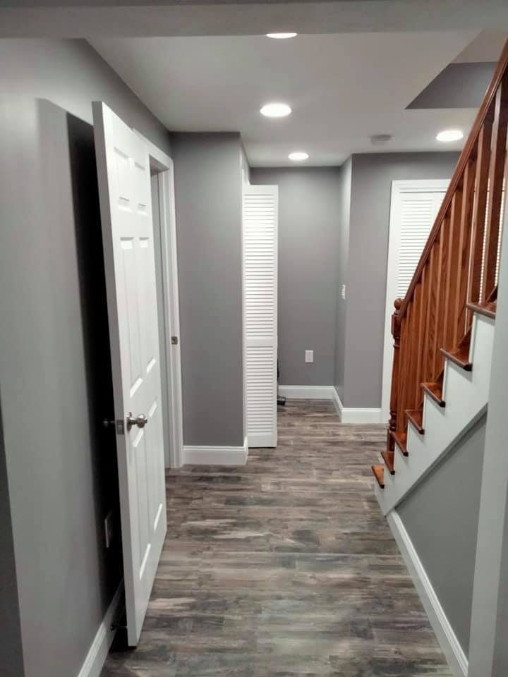 Hallway with gray walls, wood-look flooring, white doors, and a wooden staircase.