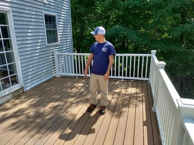 Man standing on a wooden deck next to a house with a white railing.