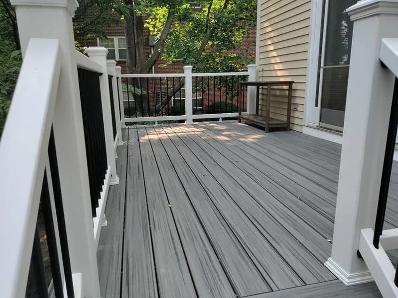 Gray composite deck with white and black railings, next to a house.