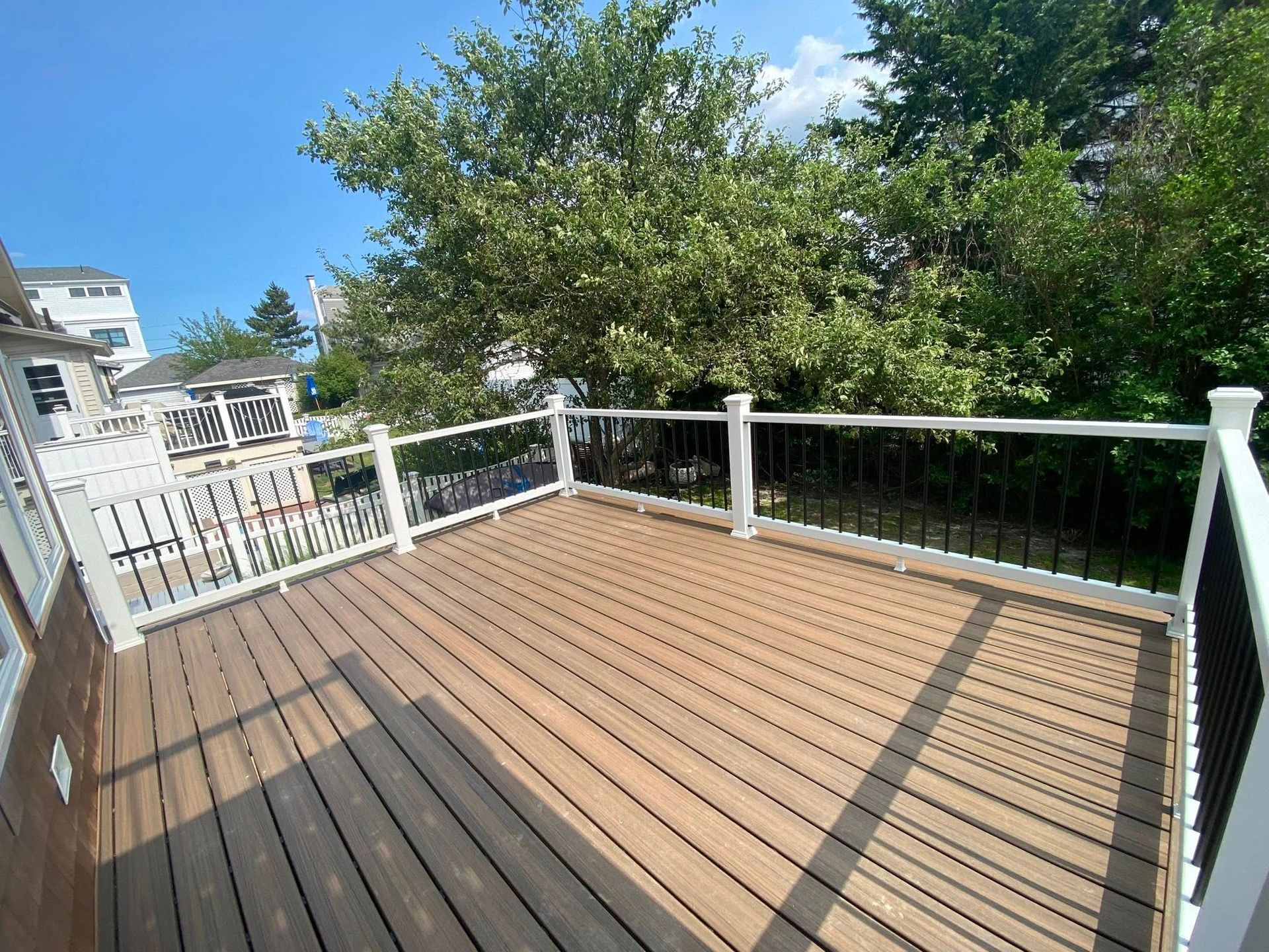 Wooden deck with white railings and black spindles, overlooking trees and a blue sky.