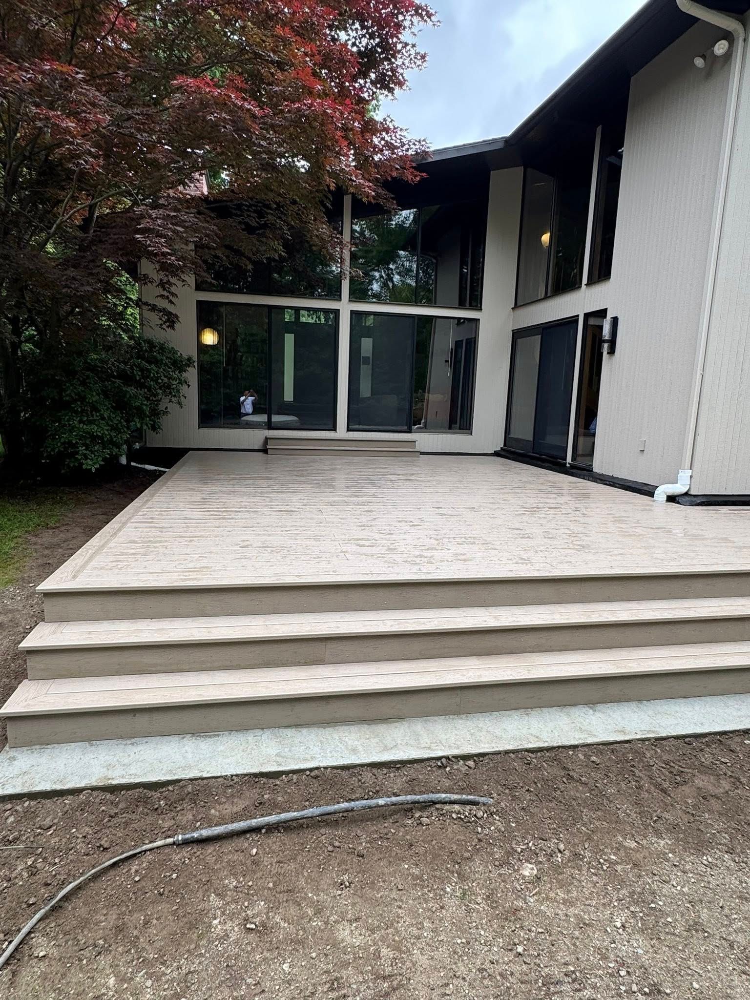 Outdoor concrete patio with steps leading to a house with large windows.