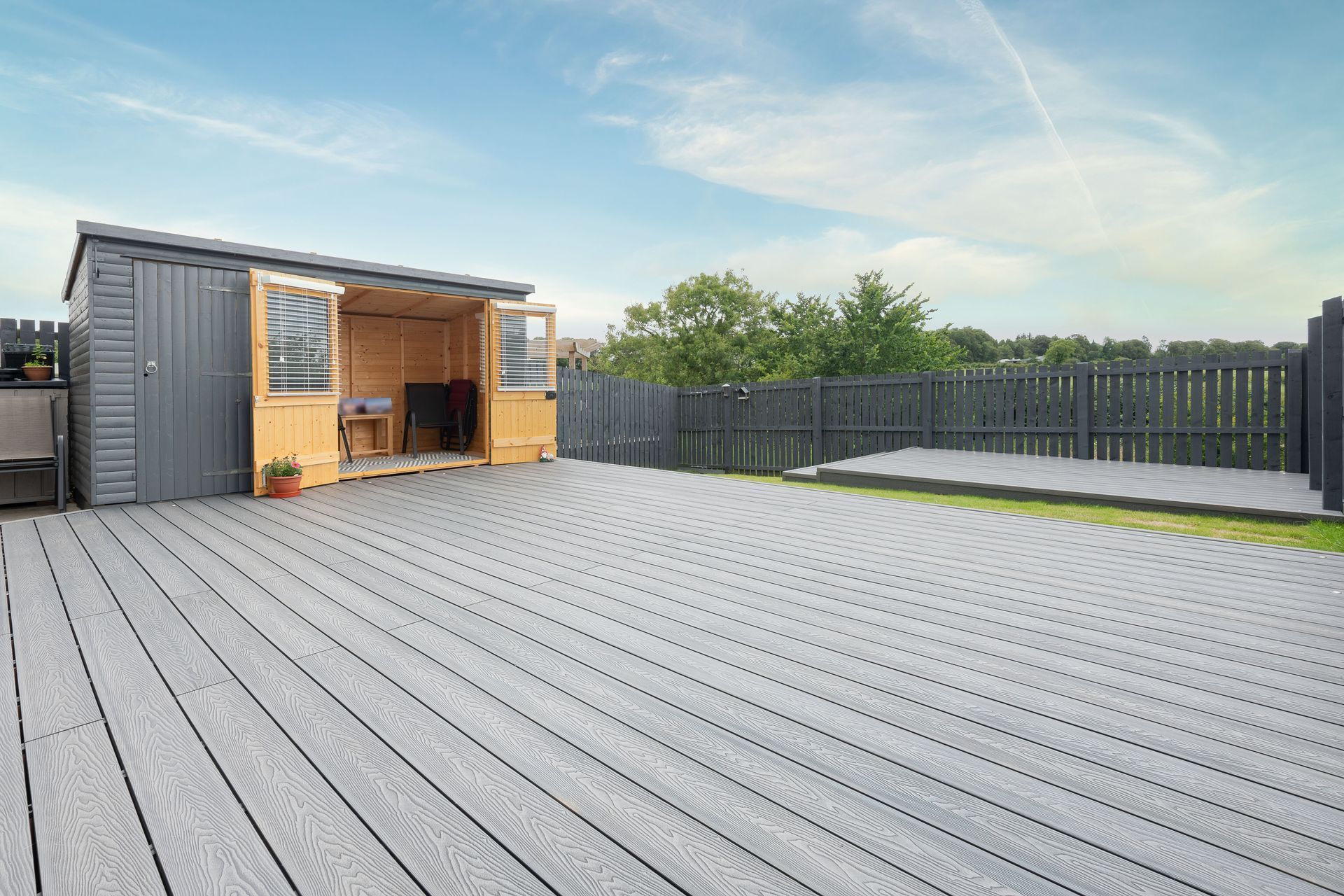 Gray composite deck with shed and fence against a blue sky.