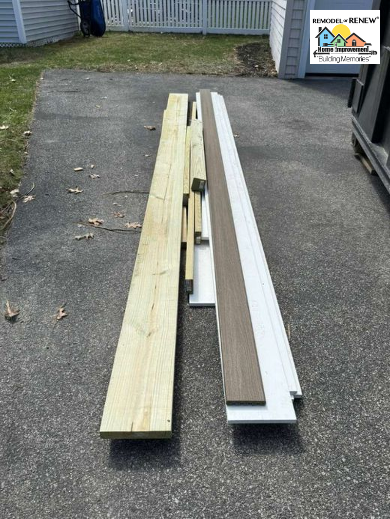 A collection of pressure-treated lumber and deck boards laid out on a paved driveway.