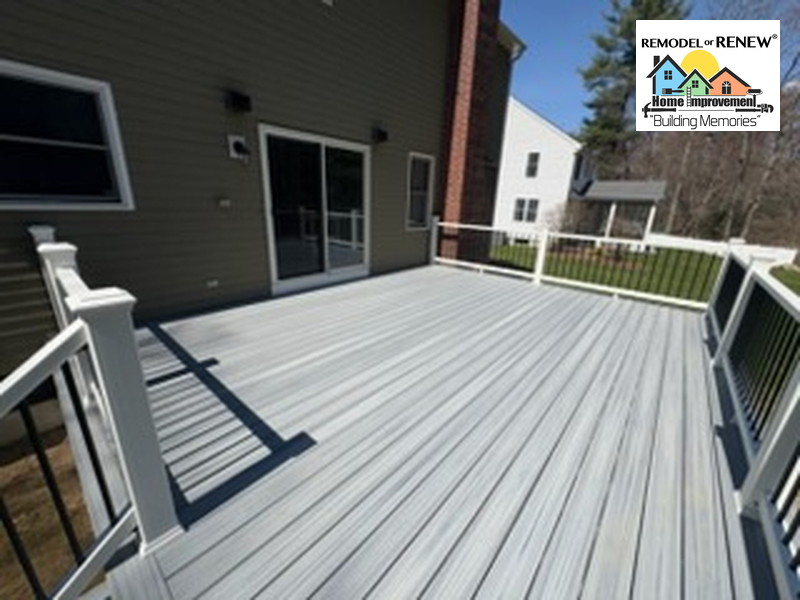 A newly constructed gray composite deck with white railings and black balusters attached to the back of a house.