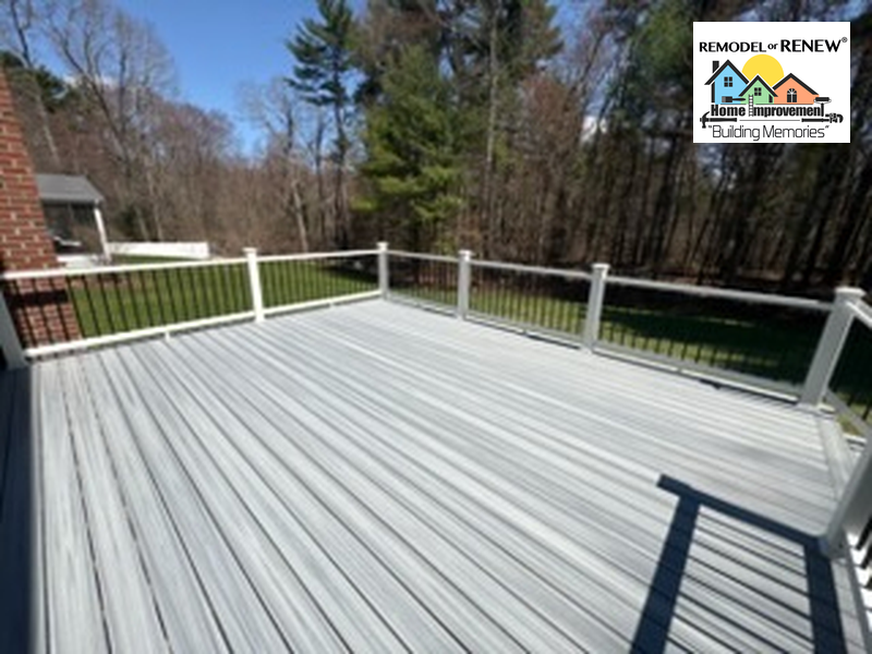 A gray composite deck with white railings and black balusters overlooking a wooded backyard on a sunny day.