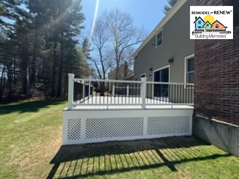 A white backyard deck with dark railings and lattice skirting attached to a gray house next to a wooded yard.