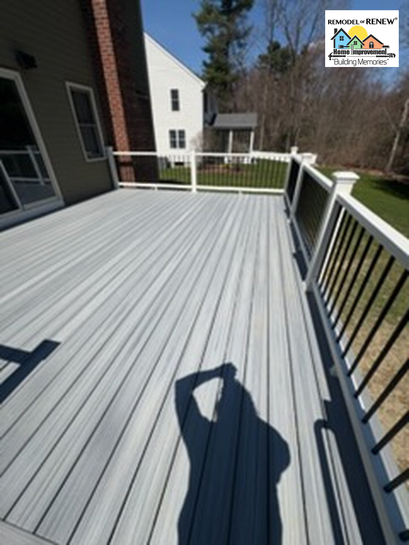 A light gray composite deck with white railings and black balusters, viewed from above with a person's shadow cast on it.
