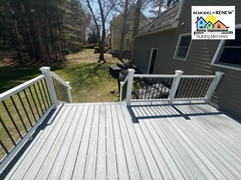 A grey composite deck with white railings and black balusters overlooks a grassy backyard.