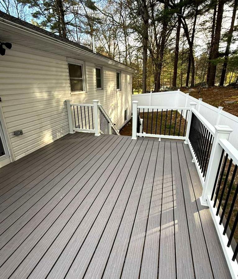 Wooden deck with white railings beside a house, overlooking trees in a wooded yard.