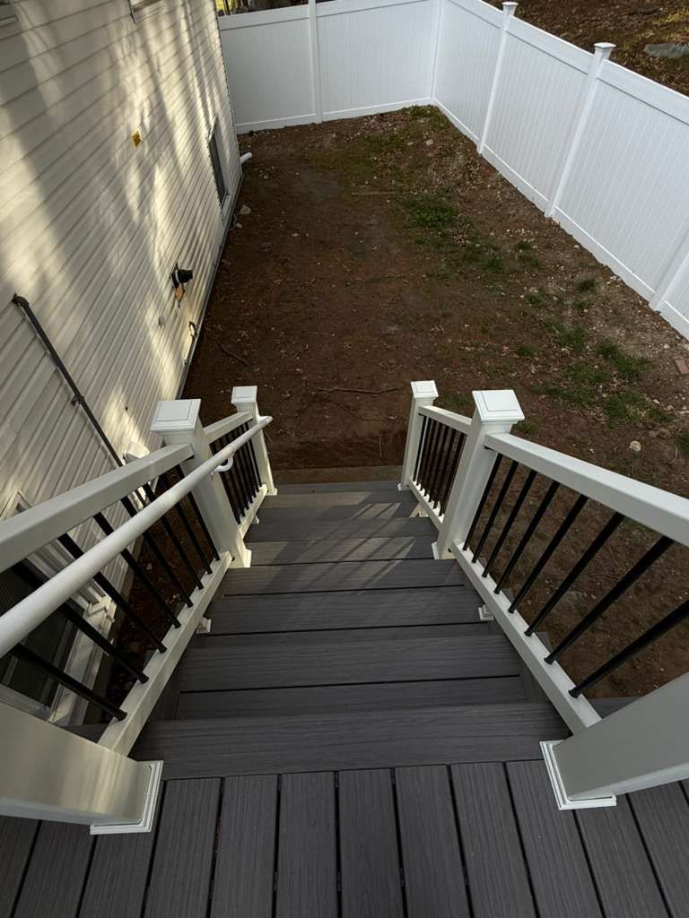Backyard stairs leading to a dirt yard, bordered by white vinyl fences and a house wall