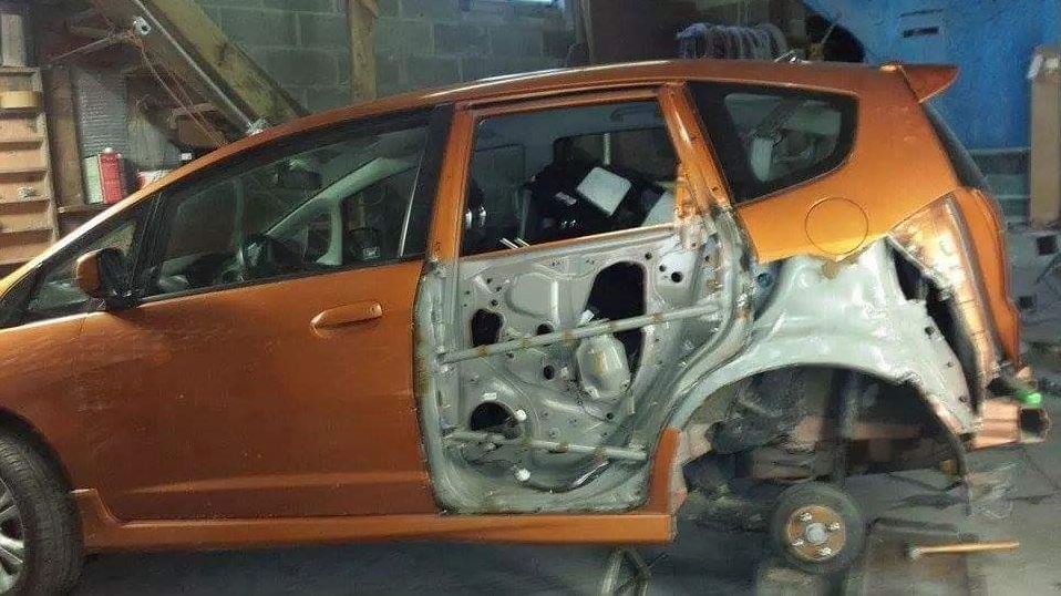 A small orange car is being dismantled in a garage.