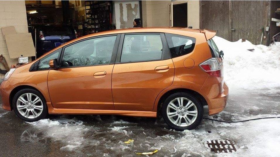 A small orange car is parked in a snowy parking lot