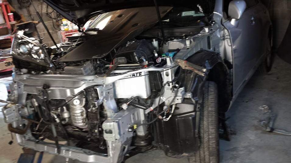 A car with the hood up is being worked on in a garage.