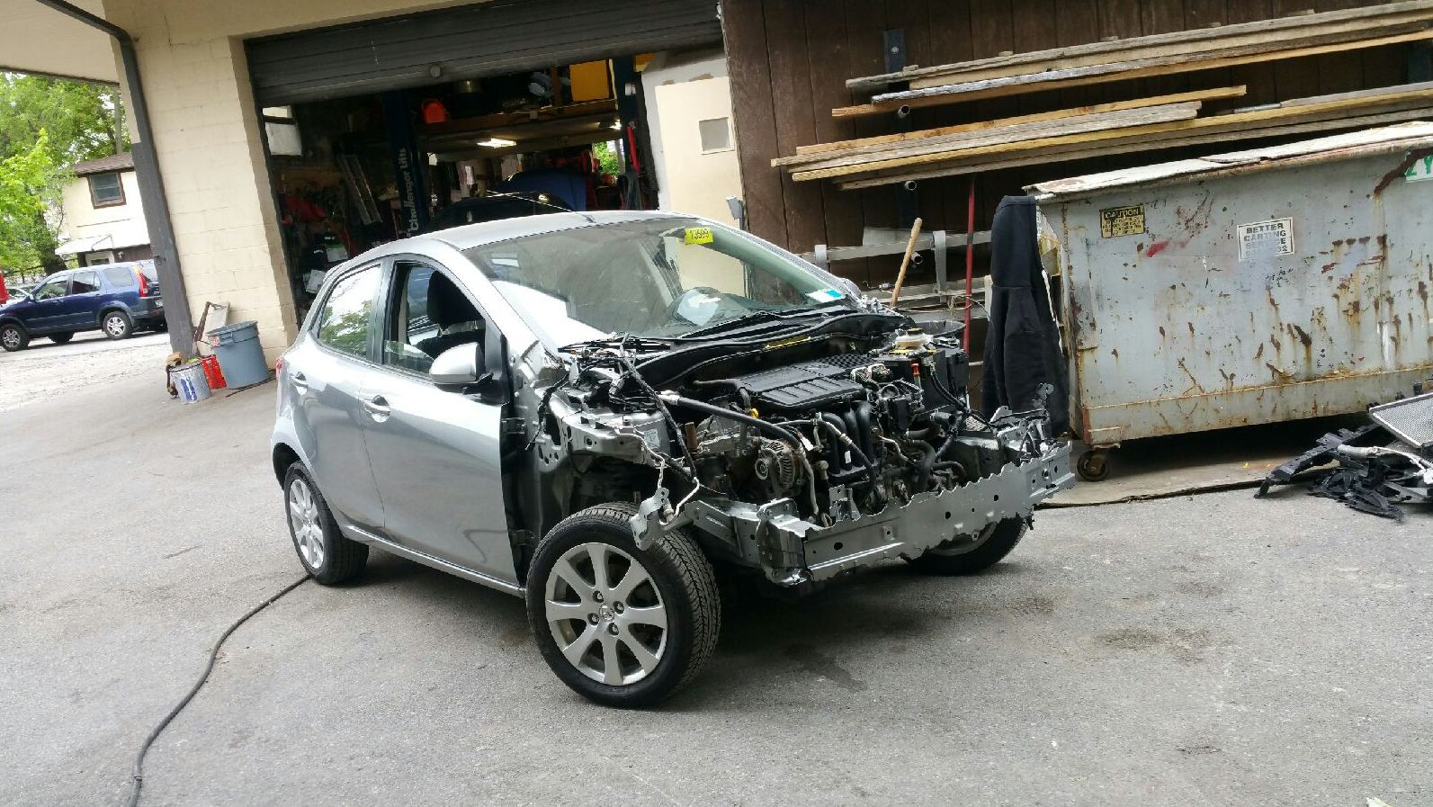 A damaged car is parked in front of a garage.