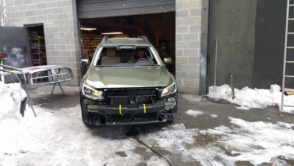 A green suv is parked in the snow in front of a garage.