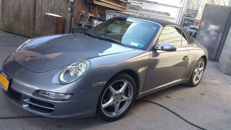A gray porsche 911 convertible is parked in a parking lot.