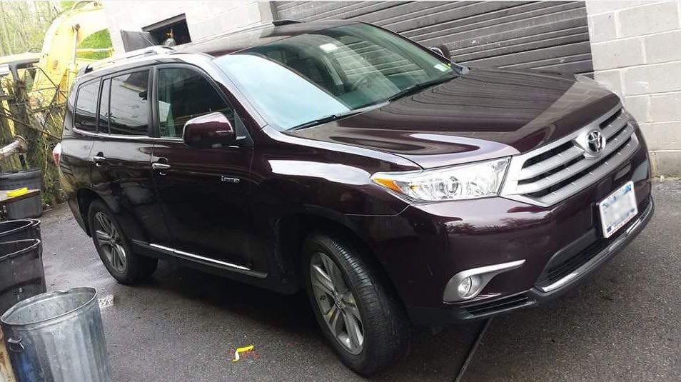 A purple toyota highlander is parked in a driveway next to a trash can.