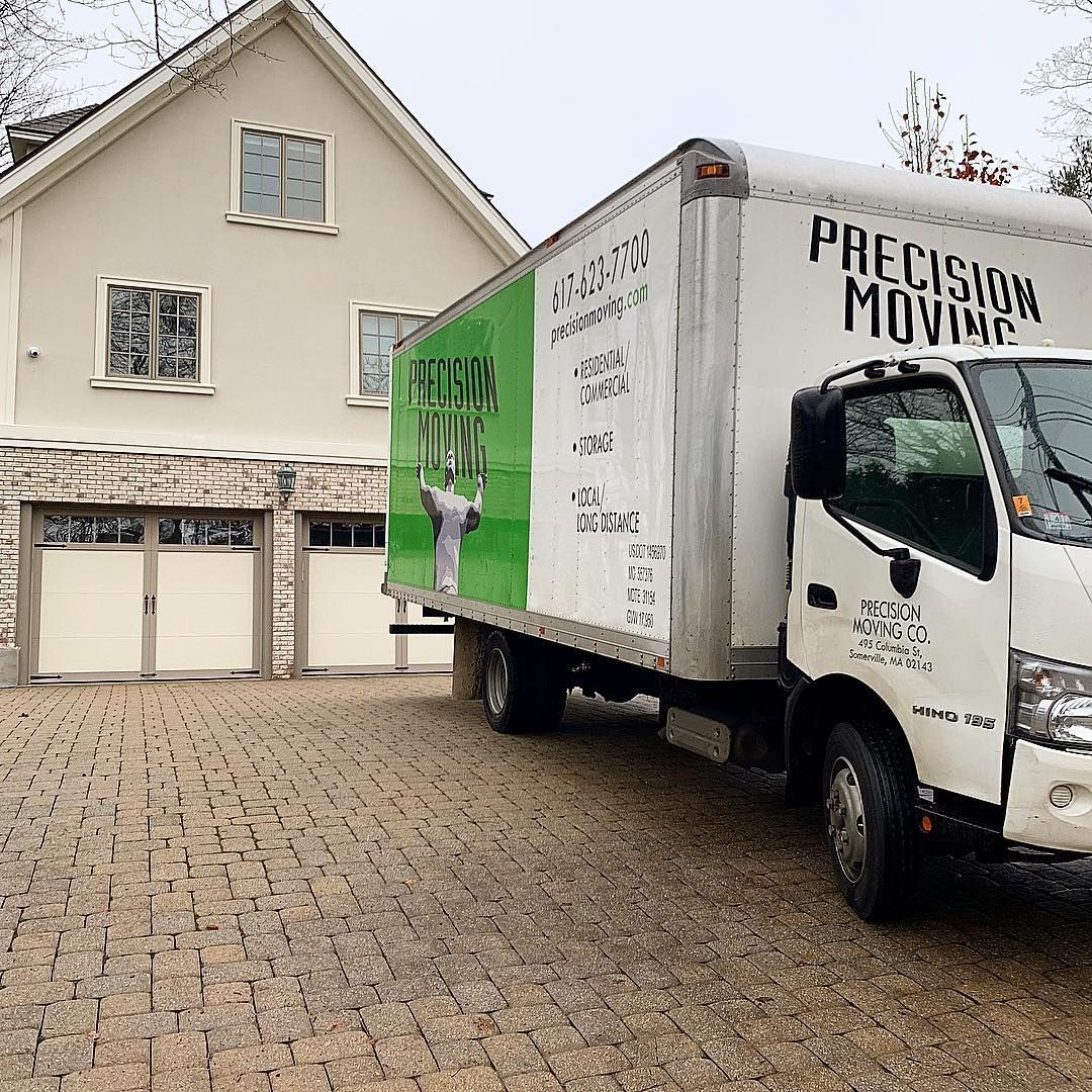 Moving truck in driveway of a light-colored house.