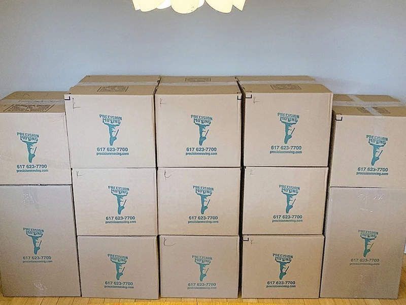 Cardboard boxes stacked against a wall; boxes have teal logos.