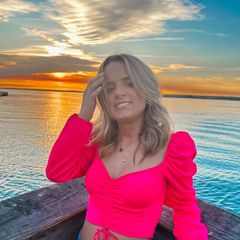 A woman in a pink crop top is sitting on a boat in the water.