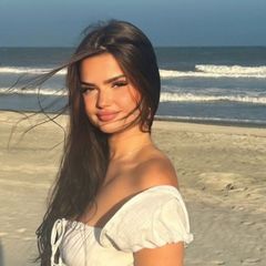 A woman in a white off the shoulder top is standing on a beach