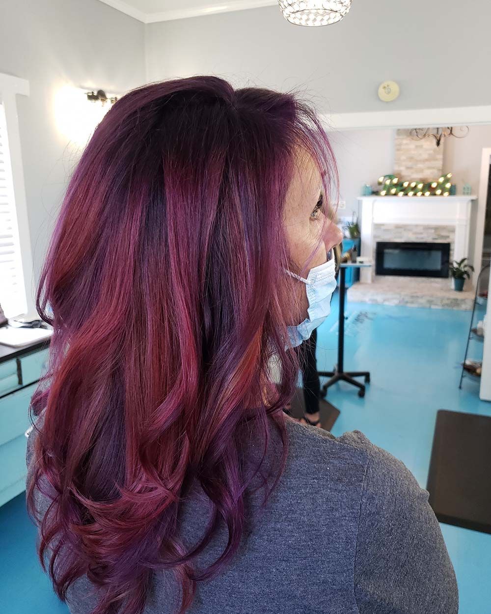 A woman with purple hair is wearing a mask in a salon.