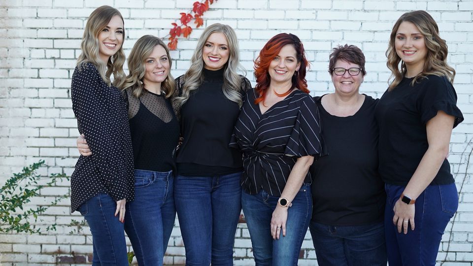 A group of women are posing for a picture in front of a white brick wall.