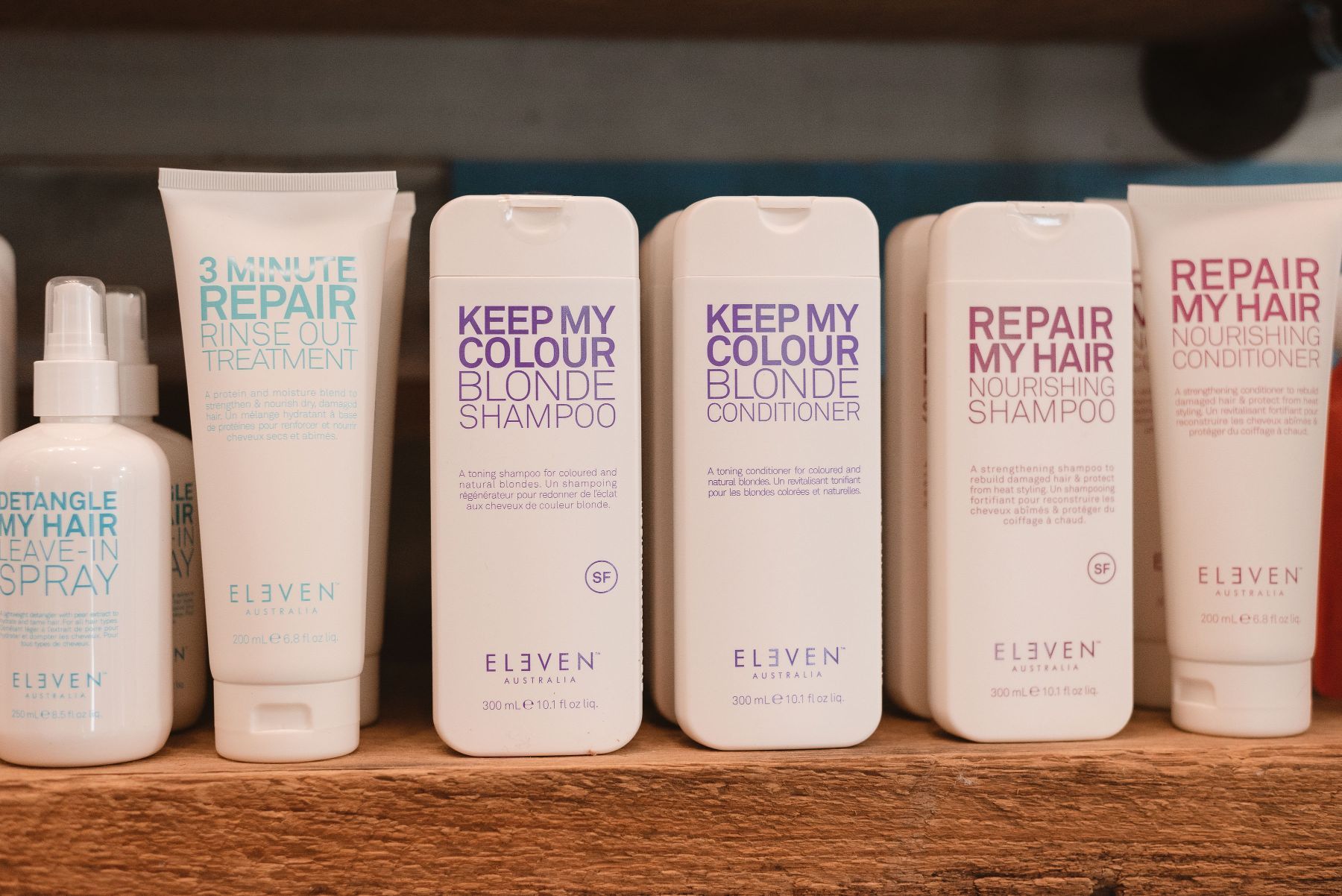 A row of eleven hair products are lined up on a wooden shelf.