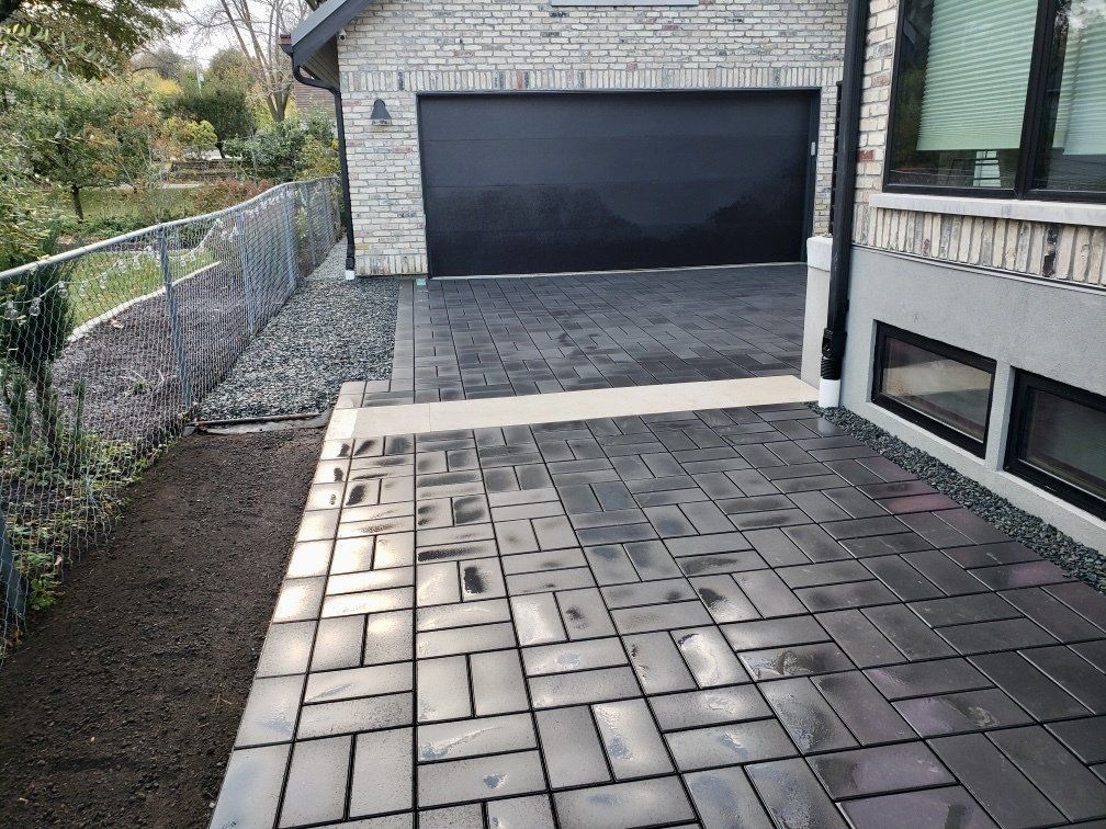 A brick driveway with a black garage door in front of a brick house.