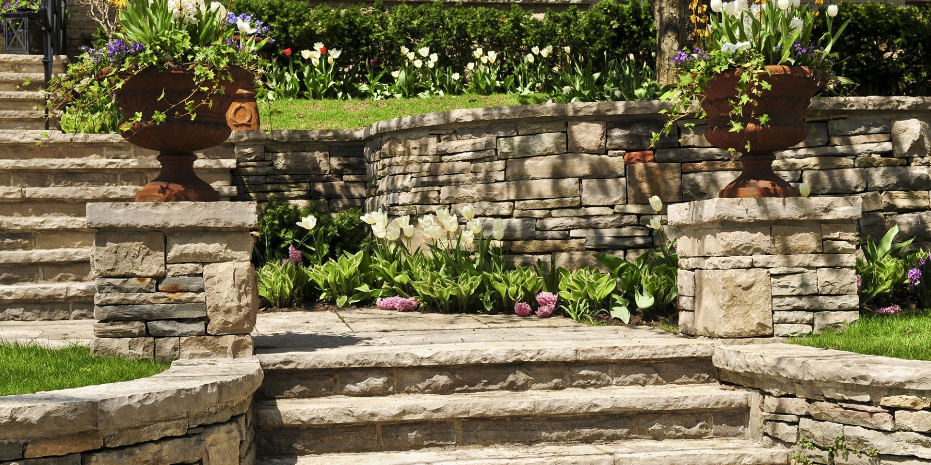 A stone wall surrounds a set of stairs in a garden.