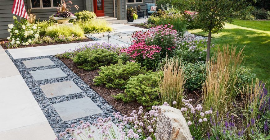 A lush green garden with flowers and rocks in front of a house.