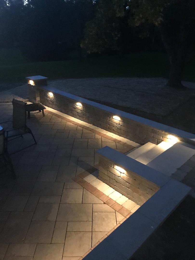 A patio with stairs and a wall with lights on it at night.
